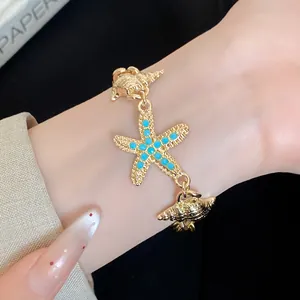 Close-up detail of a golden starfish and shell charm bracelet worn on a female wrist.
