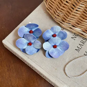 Primer plano de aretes de flores azules de gran tamaño sobre un libro de tela vintage