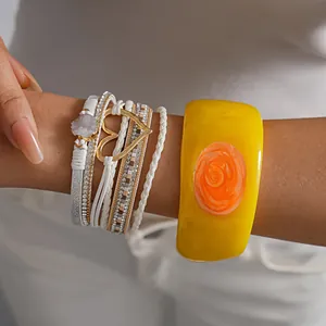 Detail of white leather heart bracelet and yellow resin bangle on wrist