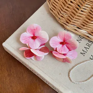 Primer plano macro de pendientes grandes de flores rosas con centro de perla roja y pétalos