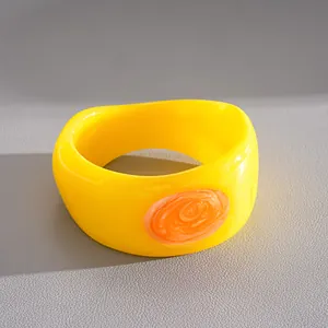 Detailed macro view of a chunky yellow resin bangle featuring a swirl orange oval accent