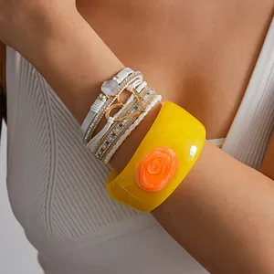 Detailed view of white leather rhinestone heart bracelet and yellow resin floral bangle