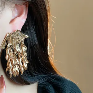 Close-up detail of elegant oversized gold wheat ear tassel earrings worn by a model