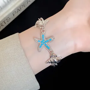 Close-up detail of a silver starfish and conch charm bracelet featuring blue beads on a wrist
