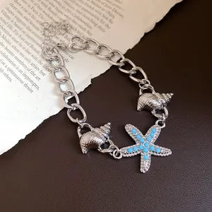 Macro detail of silver-toned chain bracelet with sea shell and blue beaded starfish charms