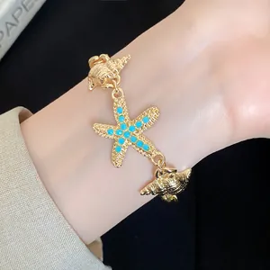 Close-up detail of a gold starfish and conch charm bracelet with blue accents on a wrist