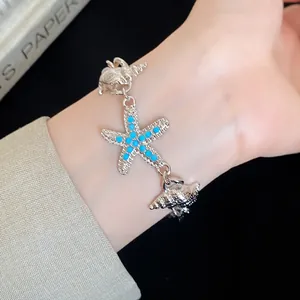 Detailed macro view of a silver starfish and conch charm bracelet worn on a female wrist.
