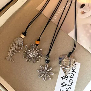 Close-up of vintage silver necklaces with fishbone and flower pendants on black cord.