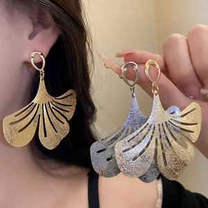 Detailed view of oversized gold and silver pleated ginkgo leaf earrings worn by model.