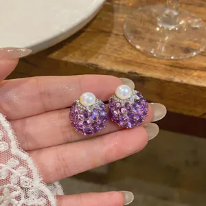 Dettaglio ravvicinato di orecchini a lobo vintage con cristalli viola e perle sulla mano