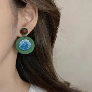Close-up view of vintage resin drop earrings with blue rose and green circular base