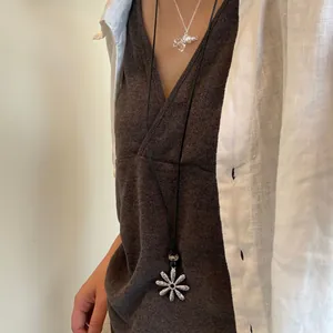 Close-up of a silver retro flower pendant on a long black cord necklace worn with linen