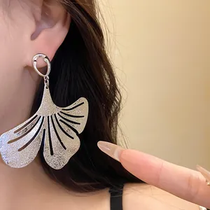 Detailed macro shot of a large silver textured ginkgo leaf dangle earring worn by a model.