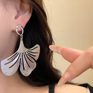 Close-up of elegant large textured silver ginkgo leaf drop earrings worn by a model