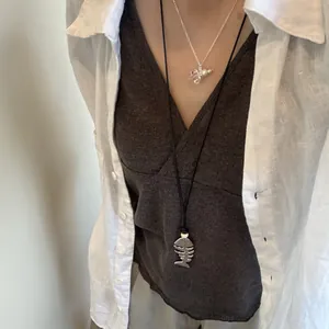 Detail view of silver fishbone beaded long necklace worn over a dark grey top