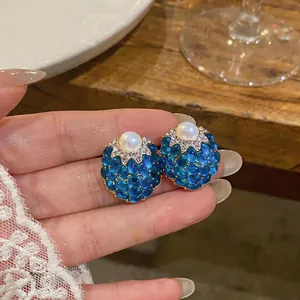 Primo piano di orecchini vintage con pietre blu, perla centrale e punti luce chiari