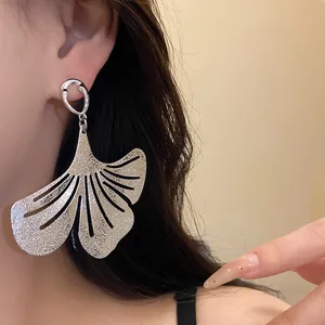 Macro detail of textured silver ginkgo leaf dangle earring worn by model in a stylish look