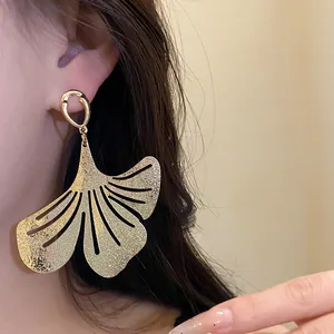 Close-up of golden vintage textured metal ginkgo leaf dangle earrings on ear