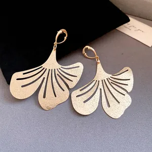Detailed macro view of golden ginkgo leaf earrings on a black velvet pouch background