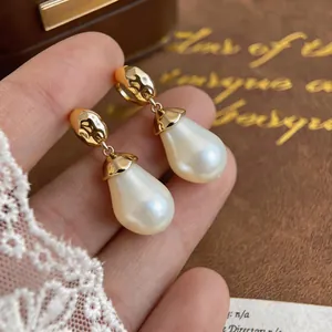 Detail of teardrop pearl earrings with hammered gold metal texture and silver needles
