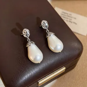 Close-up detail of elegant water drop pearl earrings with pleated silver metal accents on box