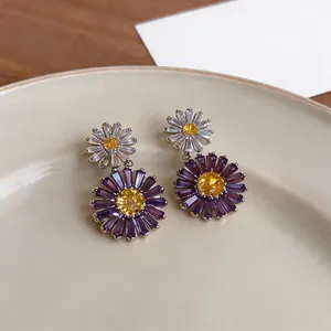 Detailed macro view of delicate zircon flower dangle earrings in purple and white tones.