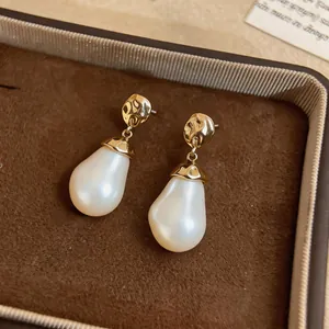 Macro view of elegant gold hammered pearl drop earrings resting on a brown velvet box.