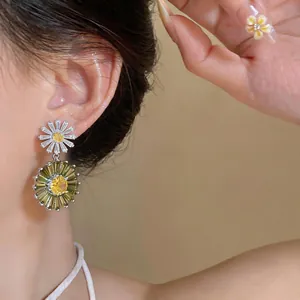 Elegant daisy drop earrings with green crystals and yellow center, close-up on model.