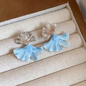Delicate ginkgo leaf stud earrings with blue drip oil enamel in a jewelry box