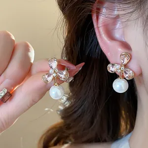 Primer plano de pendientes de flor bañados en oro con circón rosa y perlas colgantes