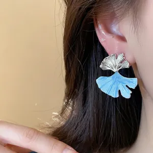 Elegant ginkgo leaf stud earrings with light blue enamel and silver needle finish.