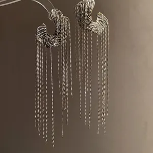 Detailed macro view of silver C-shaped earrings with long metallic bead chain fringes