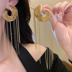 Close-up detail of golden C-shaped tassel earrings featuring long delicate bead chains