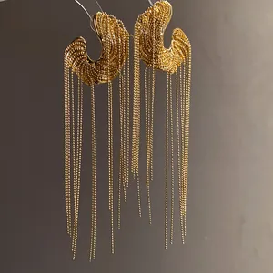 Close-up of golden C-shaped earrings featuring long delicate bead chain tassels