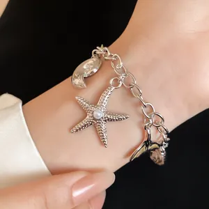 Detailed close-up of a silver charm bracelet with starfish, pearl and sea shell charms