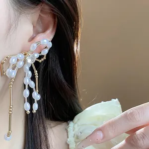 Elegant bow-shaped earrings featuring white pearls and sparkling zircons worn by a female model