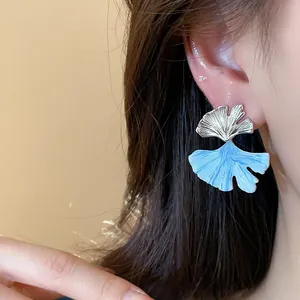 Detail view of elegant blue dripping oil ginkgo leaf earrings on a woman's ear