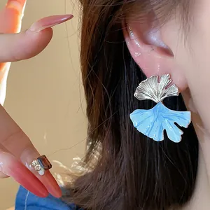 Elegant close-up of silver ginkgo leaf earrings with light blue enamel detail on ear.