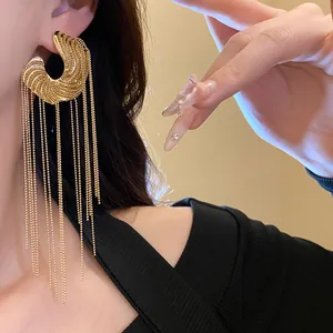 Close-up of gold C-shaped earrings with long delicate ball chain tassels on a model.