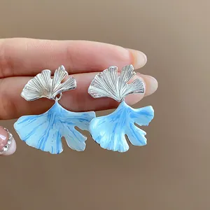 Detailed macro view of silver ginkgo leaf earrings with blue marbled enamel finish