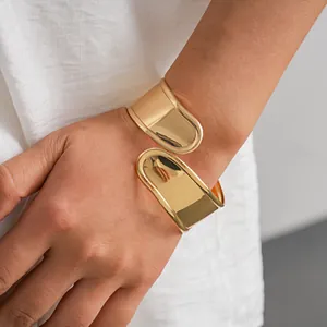 Détail d'un large bracelet manchette doré poli de forme géométrique irrégulière