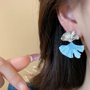Close-up of elegant ginkgo leaf earrings with blue drip oil finish on model's ear