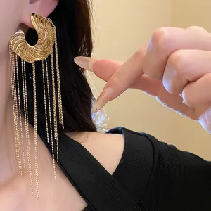 Close-up of elegant gold C-shaped earrings with long delicate ball chain tassels