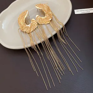 Macro view of elegant C-shaped golden tassel earrings with long beaded chains on a plate