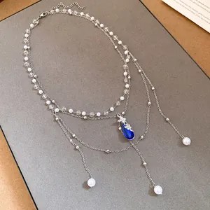 Close-up of layered pearl necklace featuring blue water-drop pendant and butterfly detail.