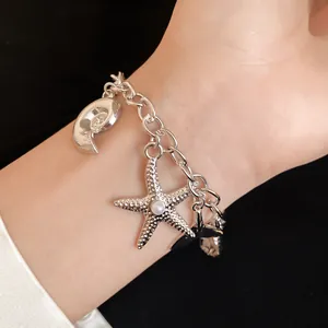 Close-up detail of a stylish silver starfish and shell charm bracelet worn on a wrist