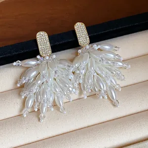 Macro view of elegant rhinestone and white pearl tassel earrings on a soft velvet display