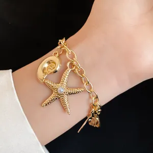 Macro view of a gold-plated charm bracelet featuring starfish and conch shell pendants