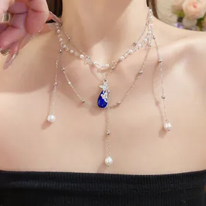 Close-up of double-layer necklace with blue water-drop pendant and butterfly details.