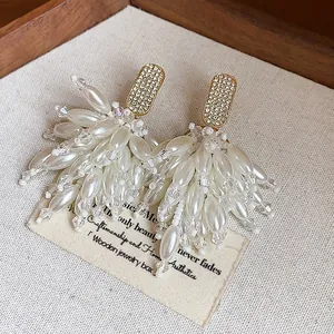Close-up of elegant rhinestone pearl tassel stud earrings on ivory display fabric